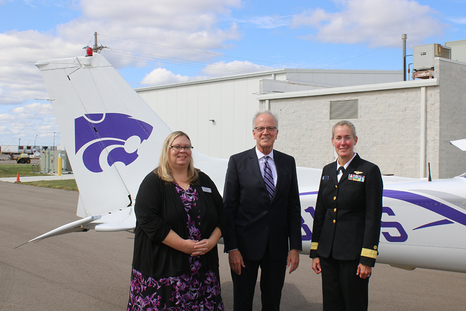 A university dean sits in a passenger seat of an airplane and displays the W-C "Wildcat" hand symbol.