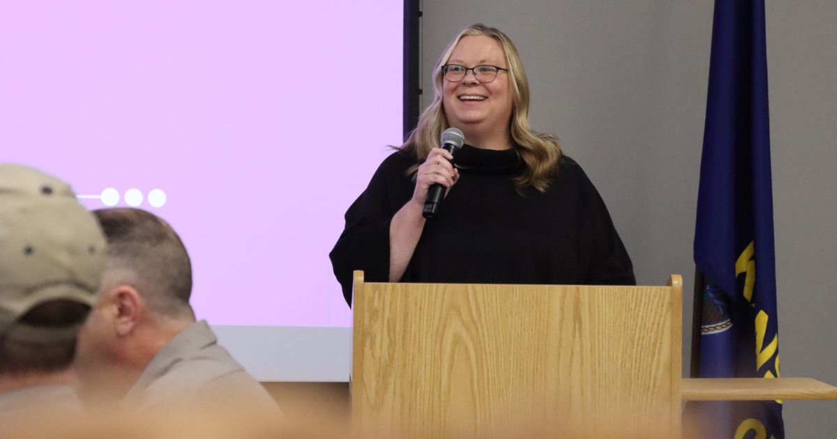 A university college dean speaks at a podium to a crowd of faculty.