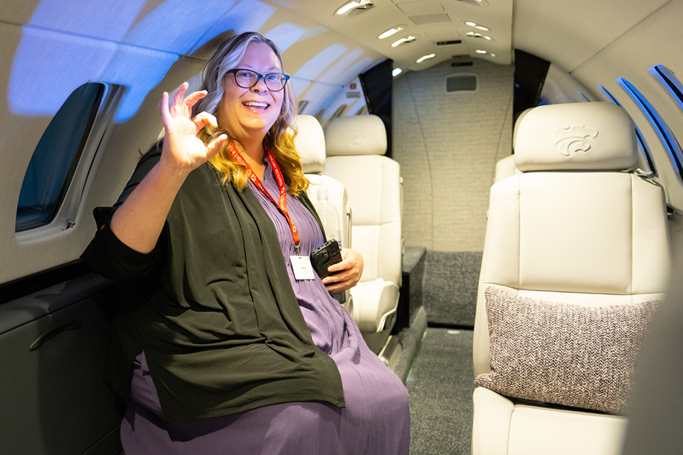 A university dean sits in a passenger seat of an airplane and displays the W-C "Wildcat" hand symbol.
