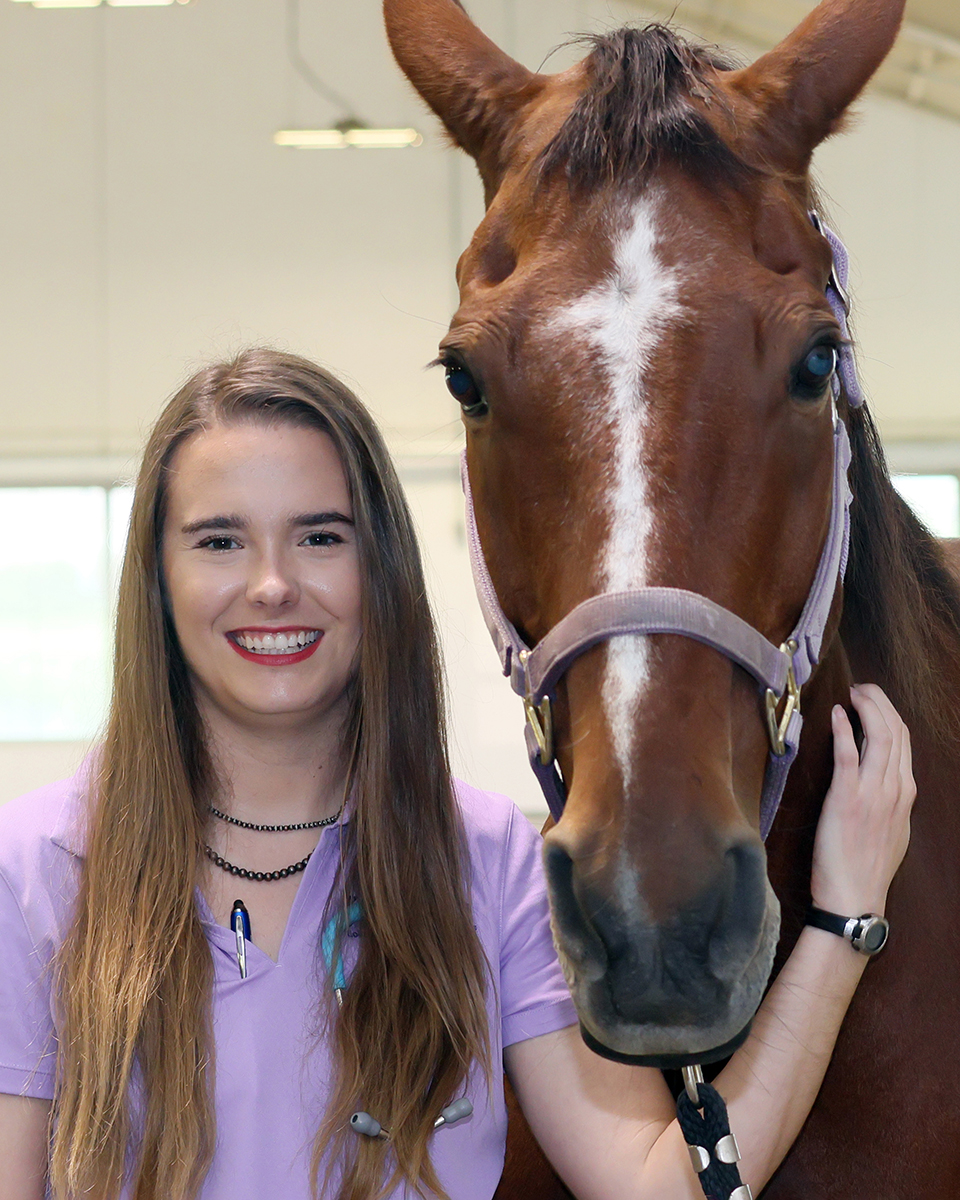 A veterinary medicine student poses for a portrait next to a horse.