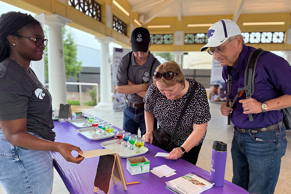 A woman stands at a table at a state fair with information and an activity for attendees at the fair. 