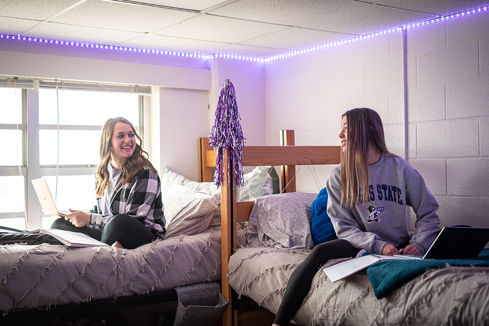 Two female college students study on the beds inside their residence hall room.