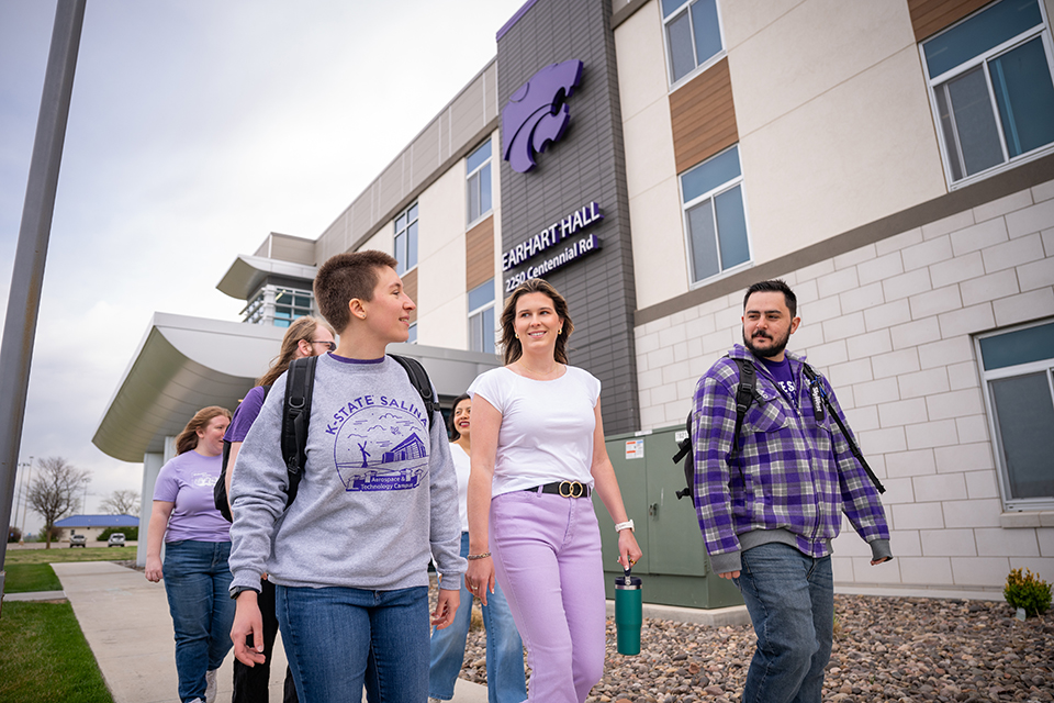 A group of college students walk outdoors in front of a residence hall.