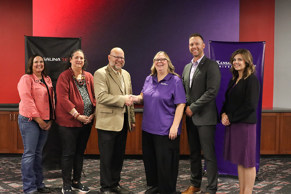A group of college administrators pose gor a group photo in a line and shake hands.