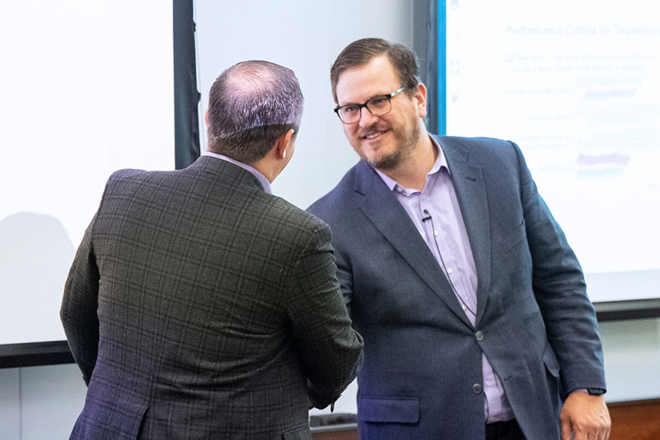A man shakes hand with a K-State professor at the front of their classroom.