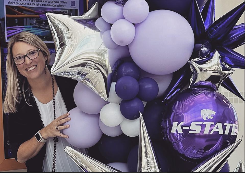 Jana Thomas smiles and peeks out behind a large bouqet of purple balloons.
