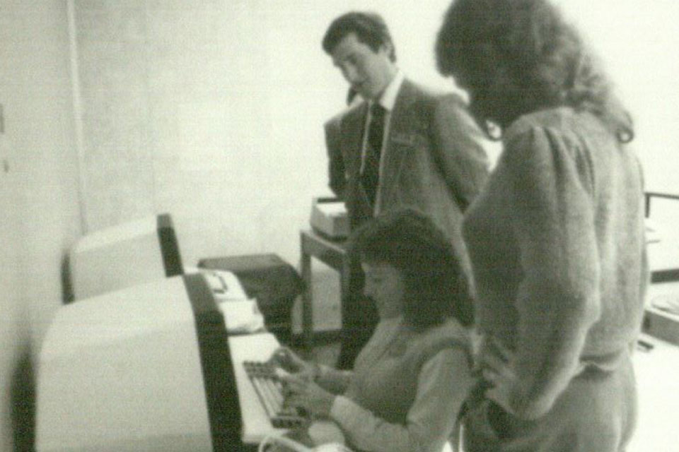 Two students listen to an instructor explain how to operate a computer.