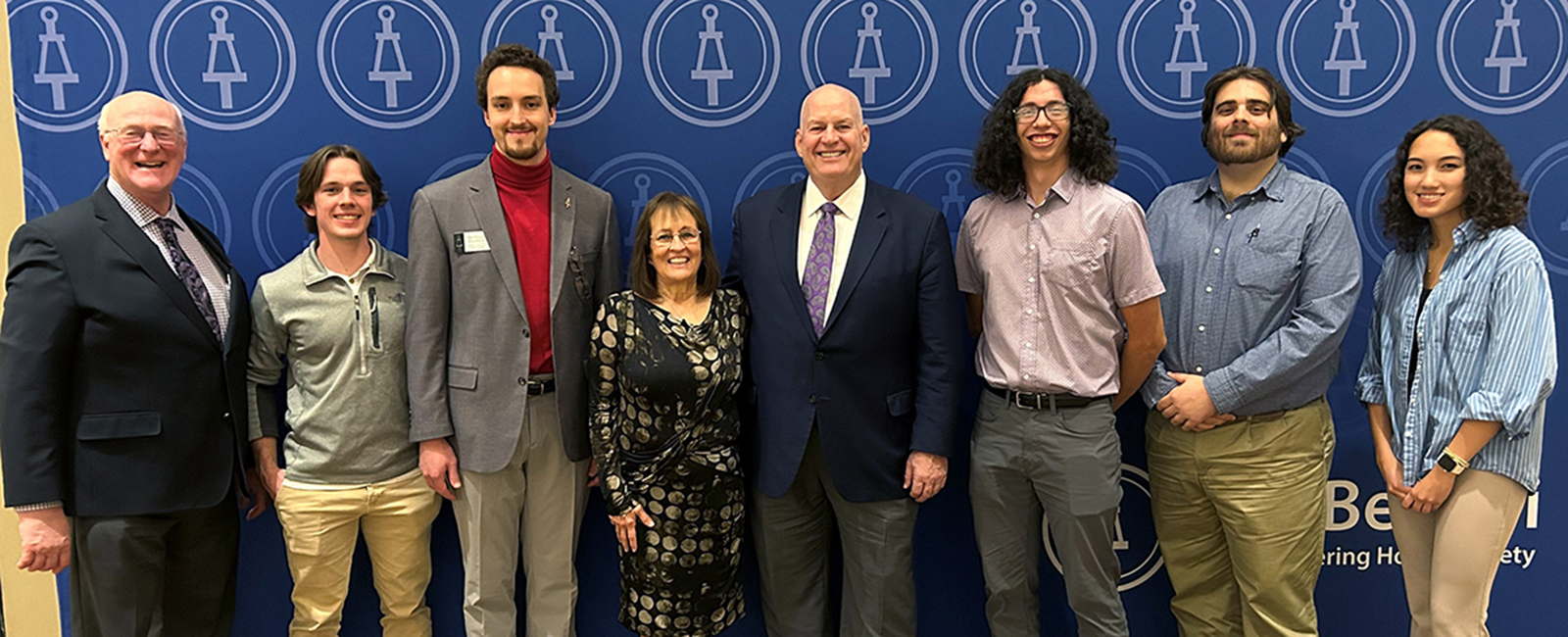 A group of college studentsand faculty pose for a group portrait in front of a blue banner in a convention center.