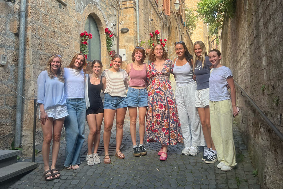 Nine women stand in a small Italian street to take a group photo