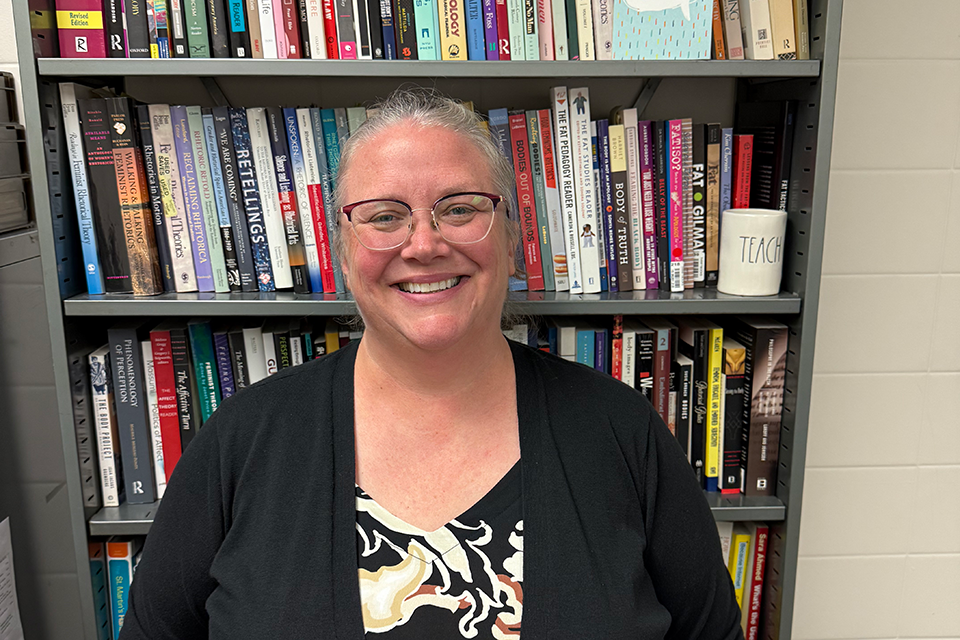 A female college professor smiles for a portrait in front of an office bookshelf.