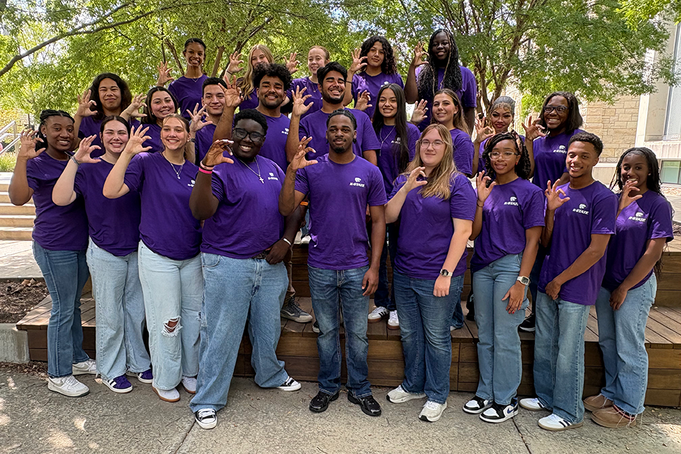 A group of college students in purple shirts pose for a group photo outside.