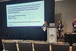 Three people stand on a stage and present at a conference.