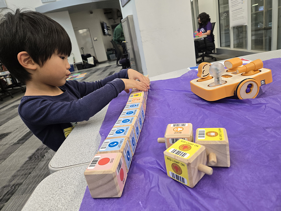 A young boy plays with computer science activities on a table with a purple cloth.