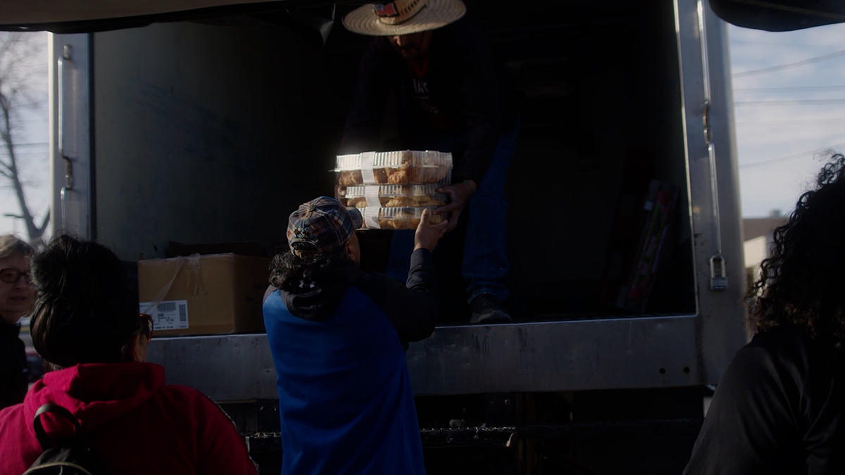 A man in a blue sweater gets food from the back of a truck.