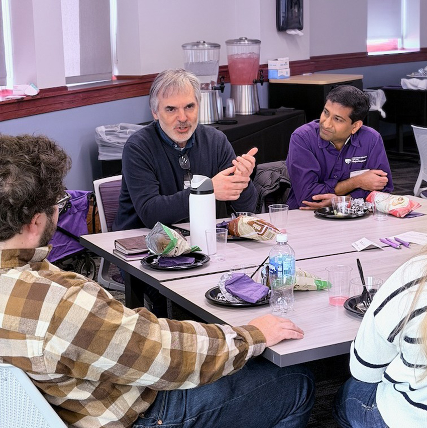 A college professor sits at a library table during a collaborative lunch and discusses water with other professors.