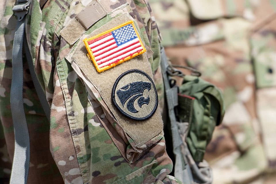 A close-up of a camo military uniform shows a backward American flag and a black Powercat silhoutte badge.