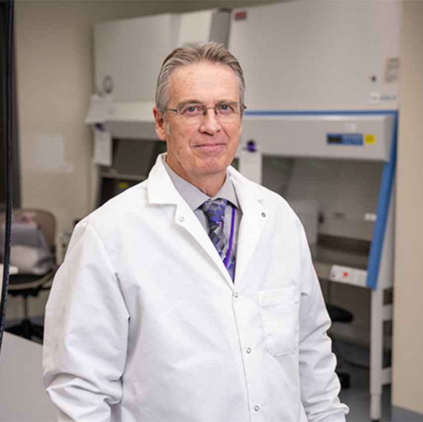 James Stack wears a white lab coat and poses for a portrait in a lab.