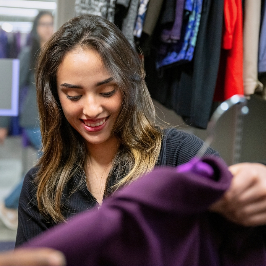 A girl smiles as she takes a hanger with a purple blazer from a staff member in the Career Closet.