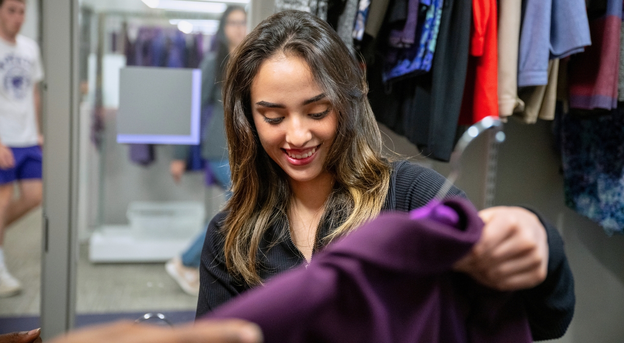 A girl smiles as she takes a hanger with a purple blazer from a staff member in the Career Closet.