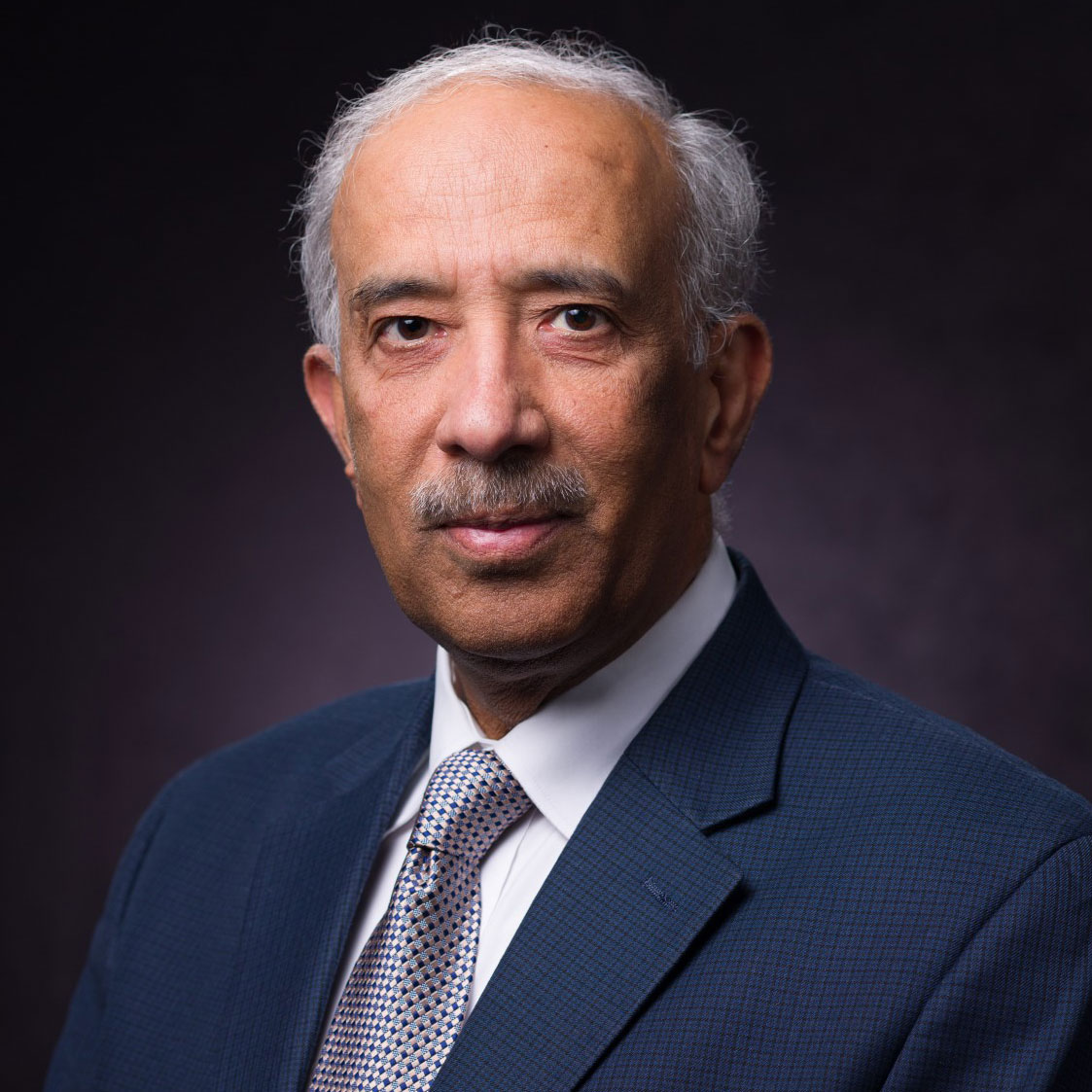 A man in a blue suit and tie smiles for a portrait image.