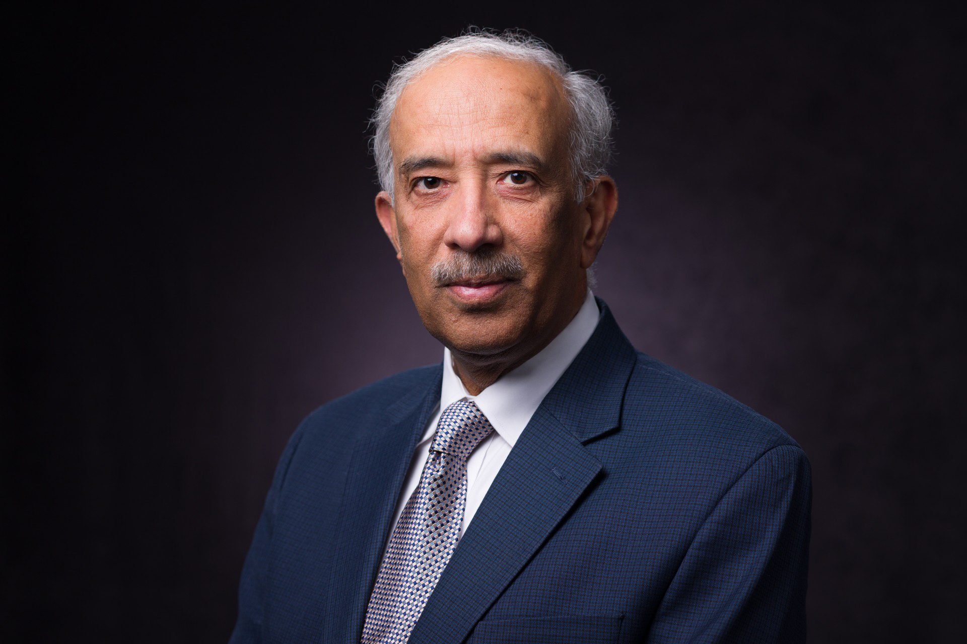 A man in a dark suit poses for a portrait.