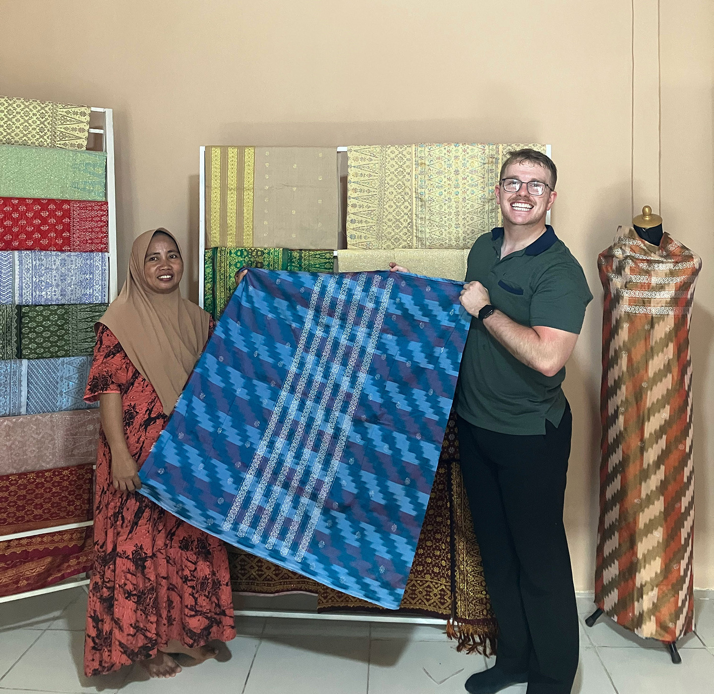 An Indonesian woman and an American college student hold a quilt up and pose for a photo.