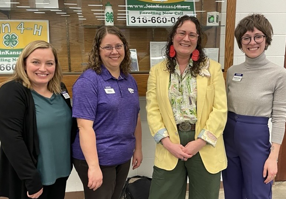 Four women stand in a college hallway and pose for a group photo.