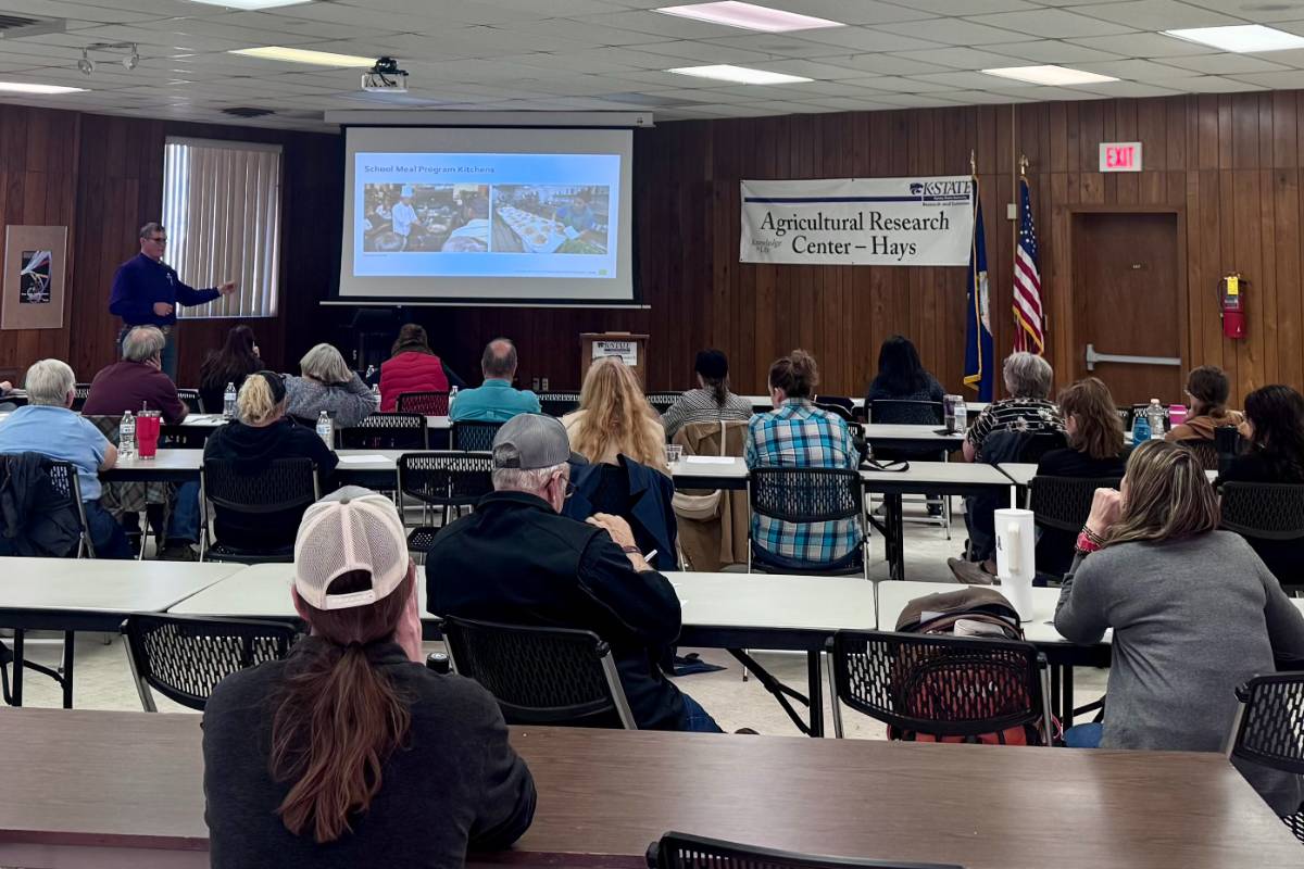 Several food business entrepreneurs sit at wooden tables in a conference room and watch a Powerpoint presentation.