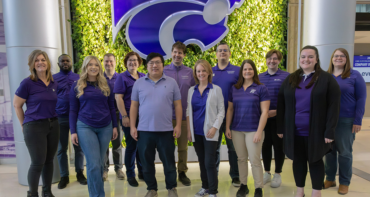A group of ten academic advisors stand together for a photo in front of a living, green wall with a large purple Powercat logo hanging from the wall.