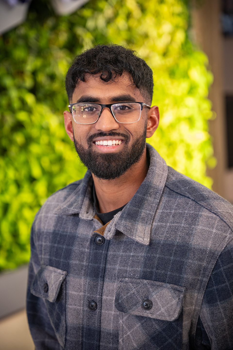 A male student in a plaid jacket smiles for a portrait image.