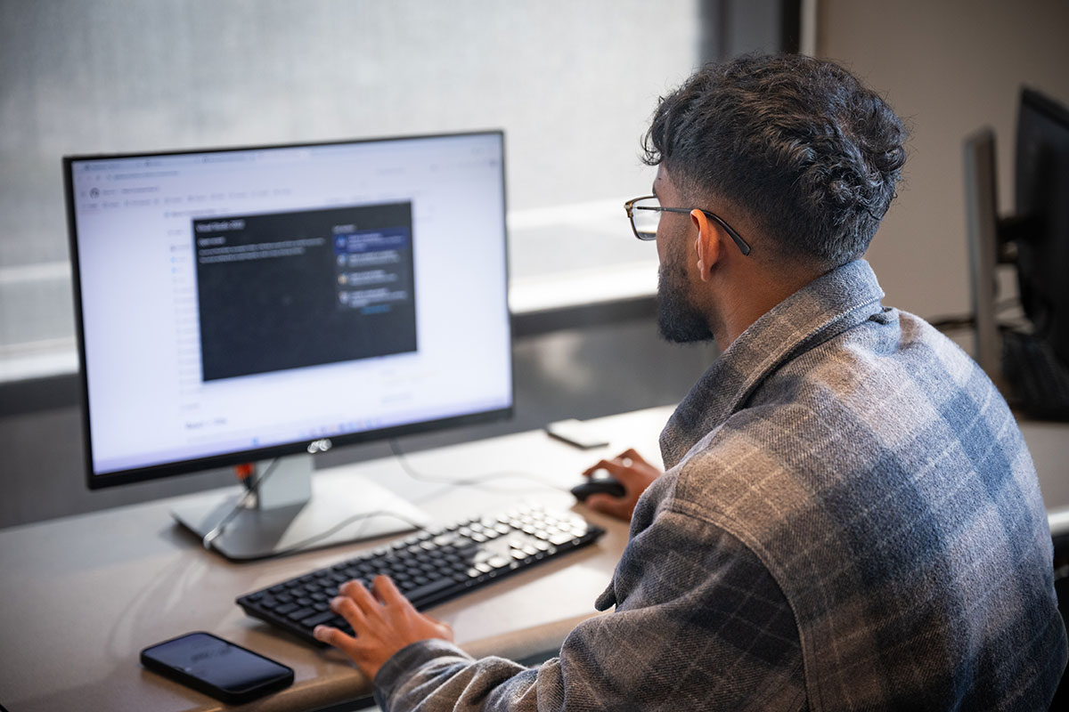 A male student in a plaid jacket types on a computer.