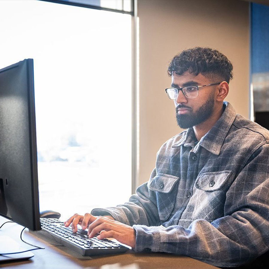 A male student in a plaid jacket types on a computer. 