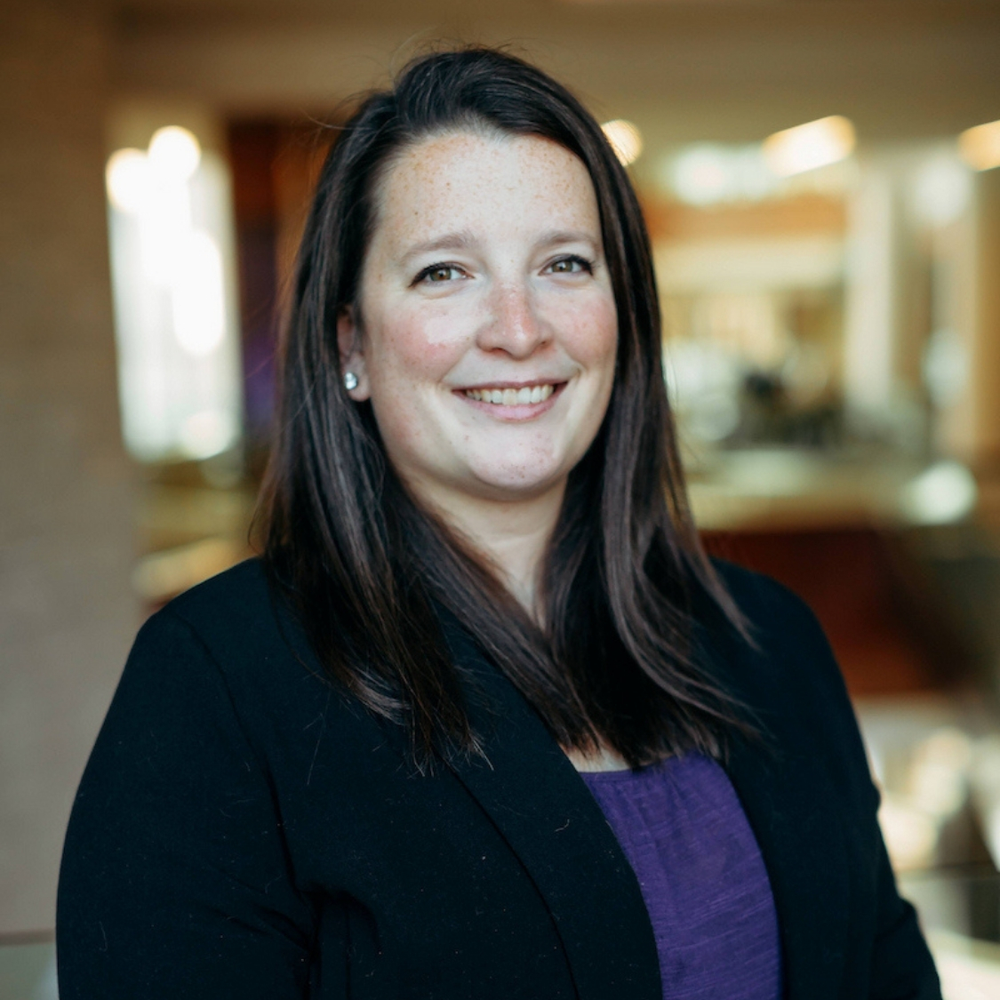 Megan Ronnebaum, wearing a purple shirt and black blazer, poses for a headshot in the K-State College of Business.