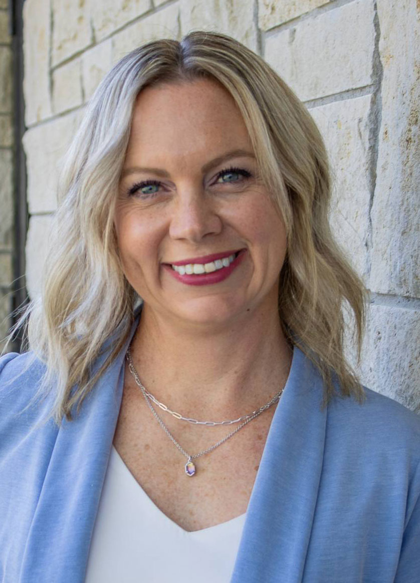 A woman in a blue blazer smiles for a portrait in front of a limestone wall.