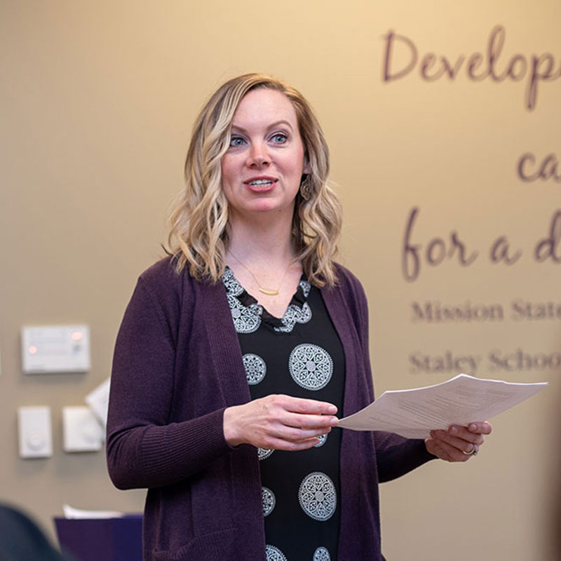 A woman in a purple cardigan speaks in front of a class. 