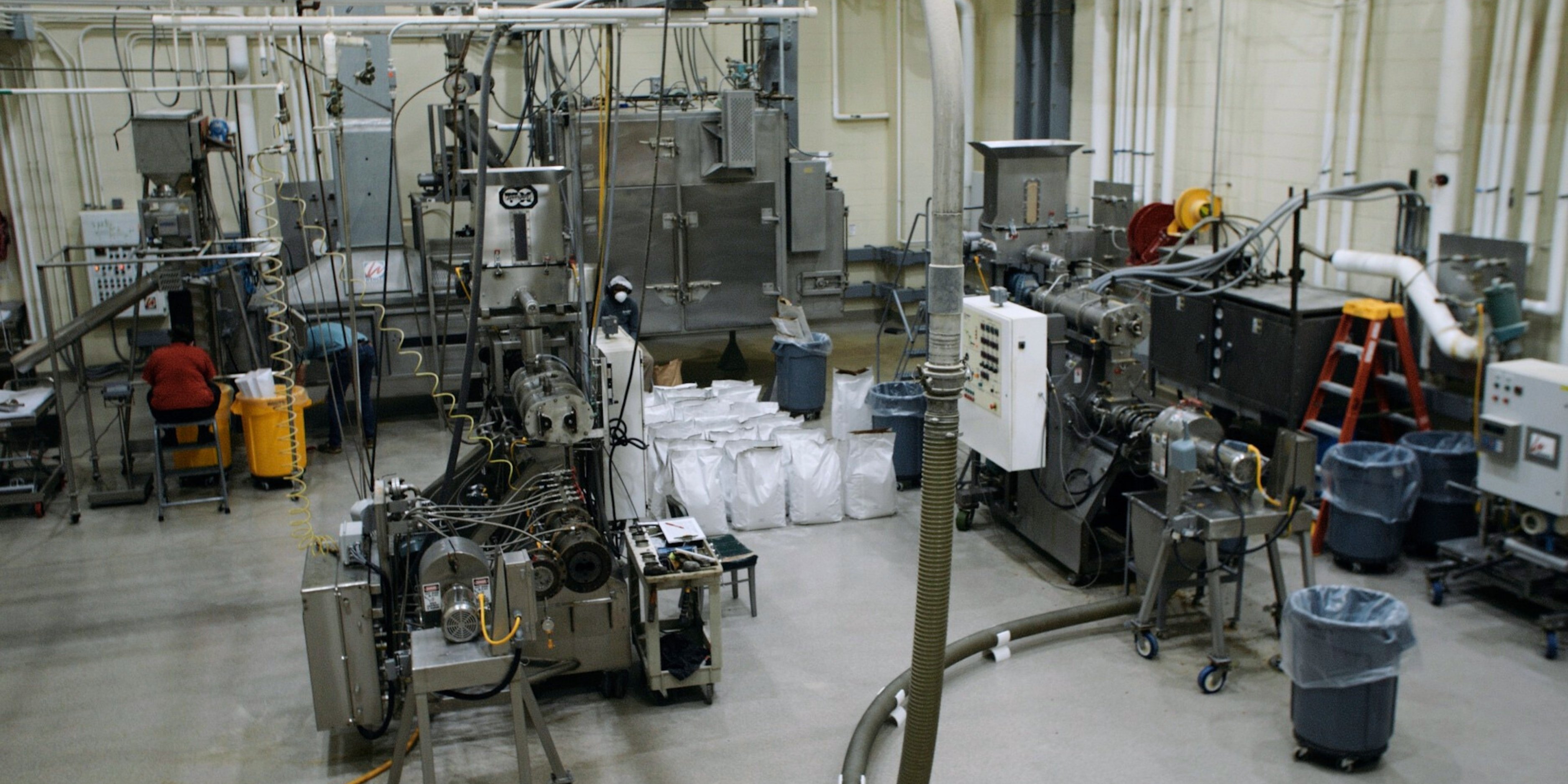 An interior aerial shot of the BIVAP facility. There is large metal machinery and large, white bags of pet food on the floor.