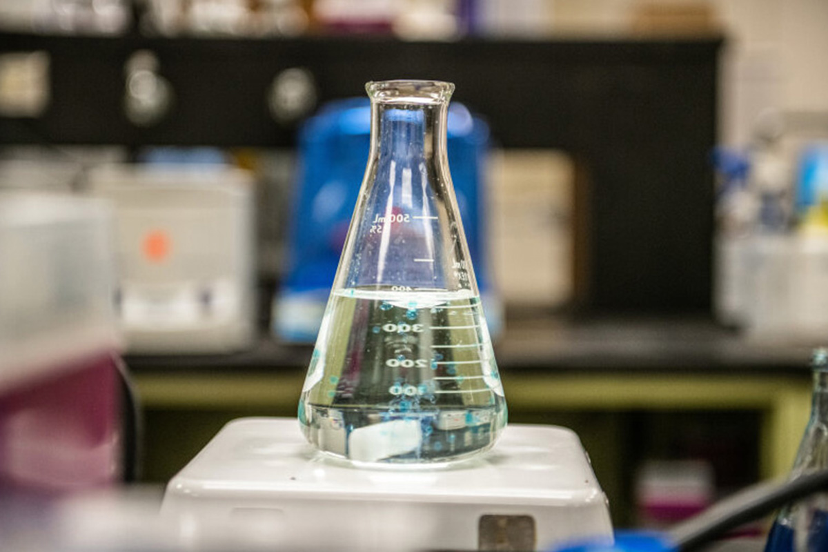 A beaker filled with liquid sits on top of a white scale with a lab background visible.