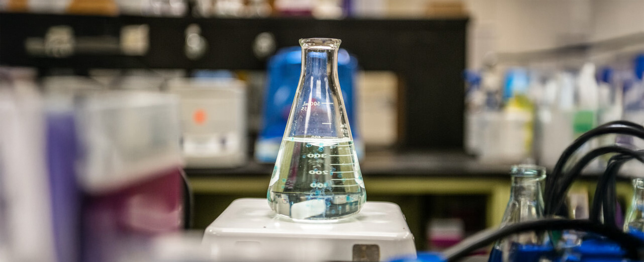 A beaker filled with liquid sits on top of a white scale with a lab background visible.