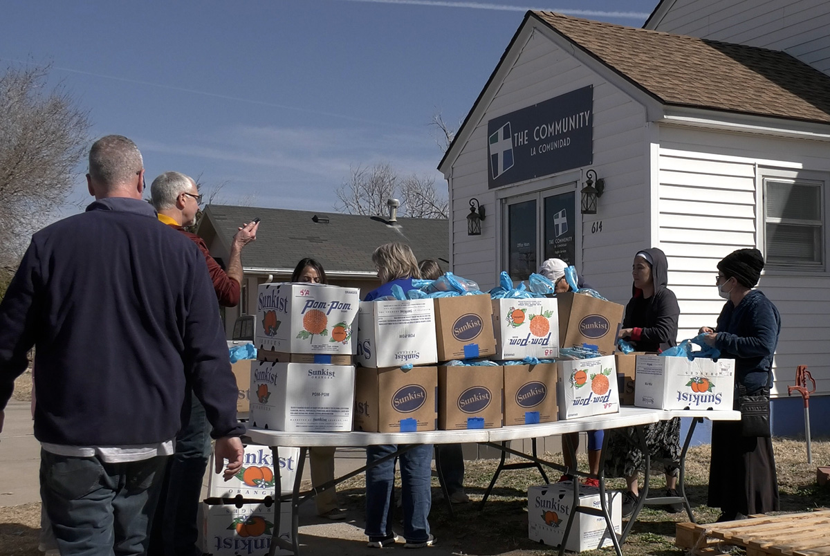 A table set up outside of a church holds boxes of food with volunteers standing around it. 