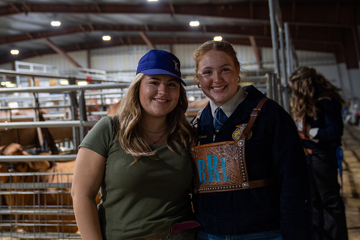 Two female college students stand in a rodeo arena. 