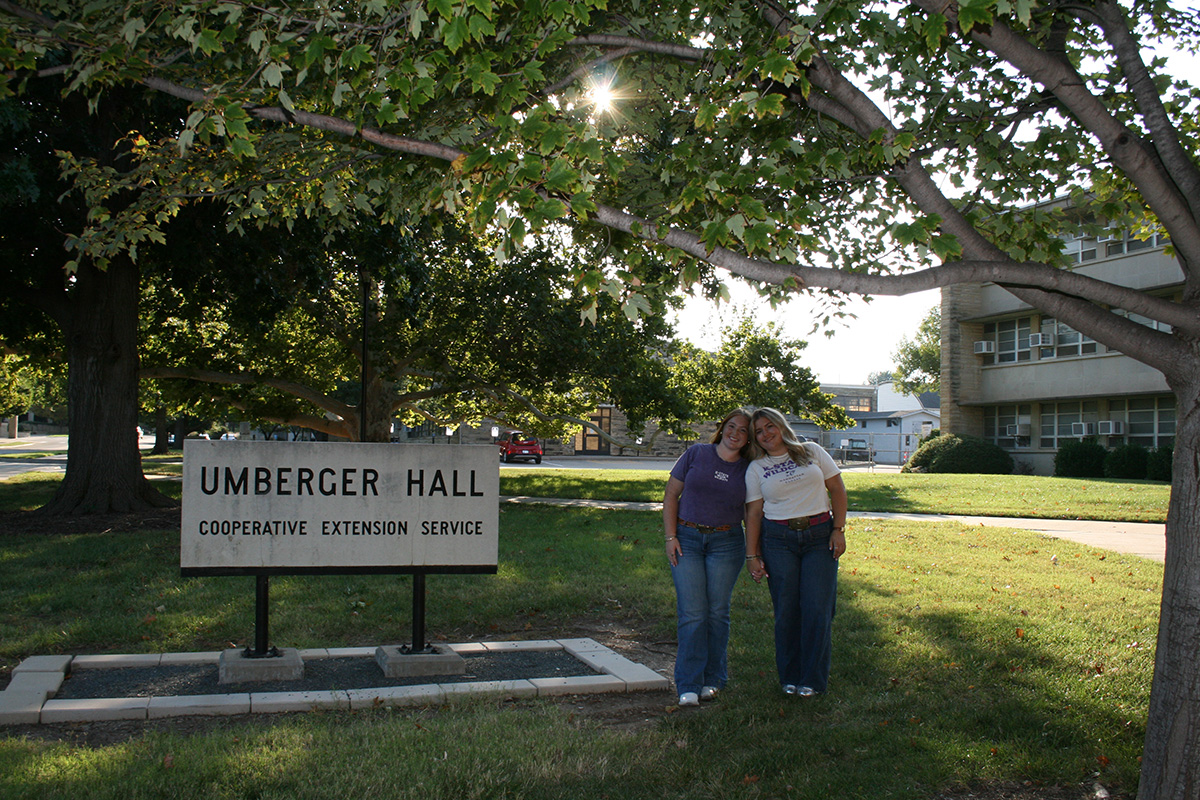 Two college students who are sisters stand together outside of Umberger Hall on the K-State campus. 