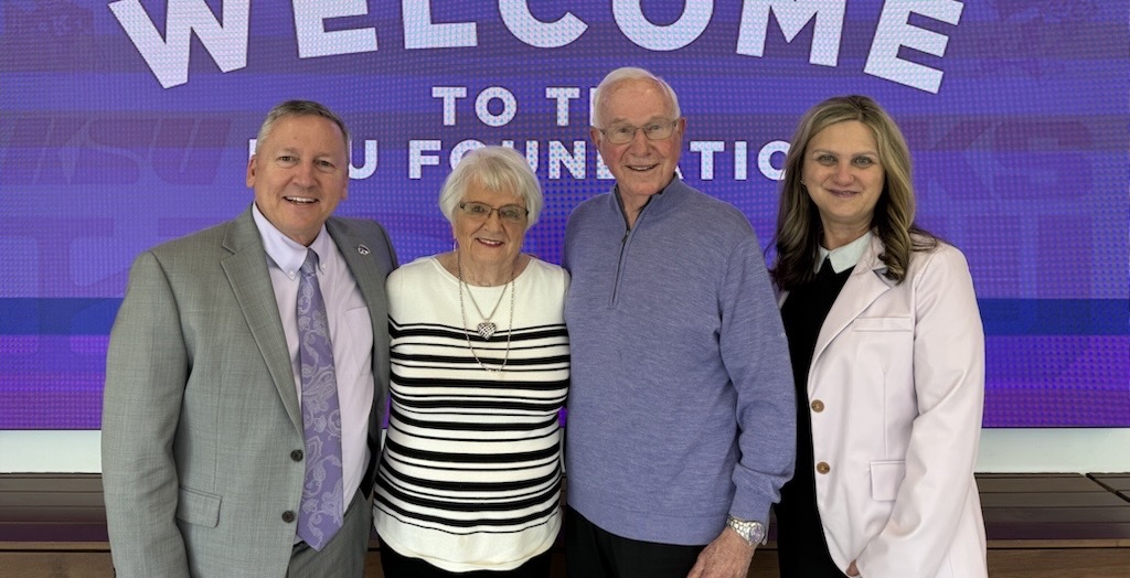 From left to right, Richard Linton, Marilyn Galle, Nelson Galle and Debbie Mercer pose for a photo. In the background, a digital screen reads "Welcome to the KSU Foundation."