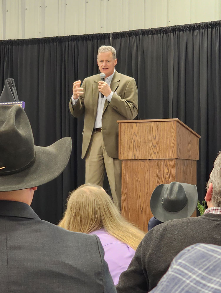 A man in a suit speaks on a stage in front of an audience