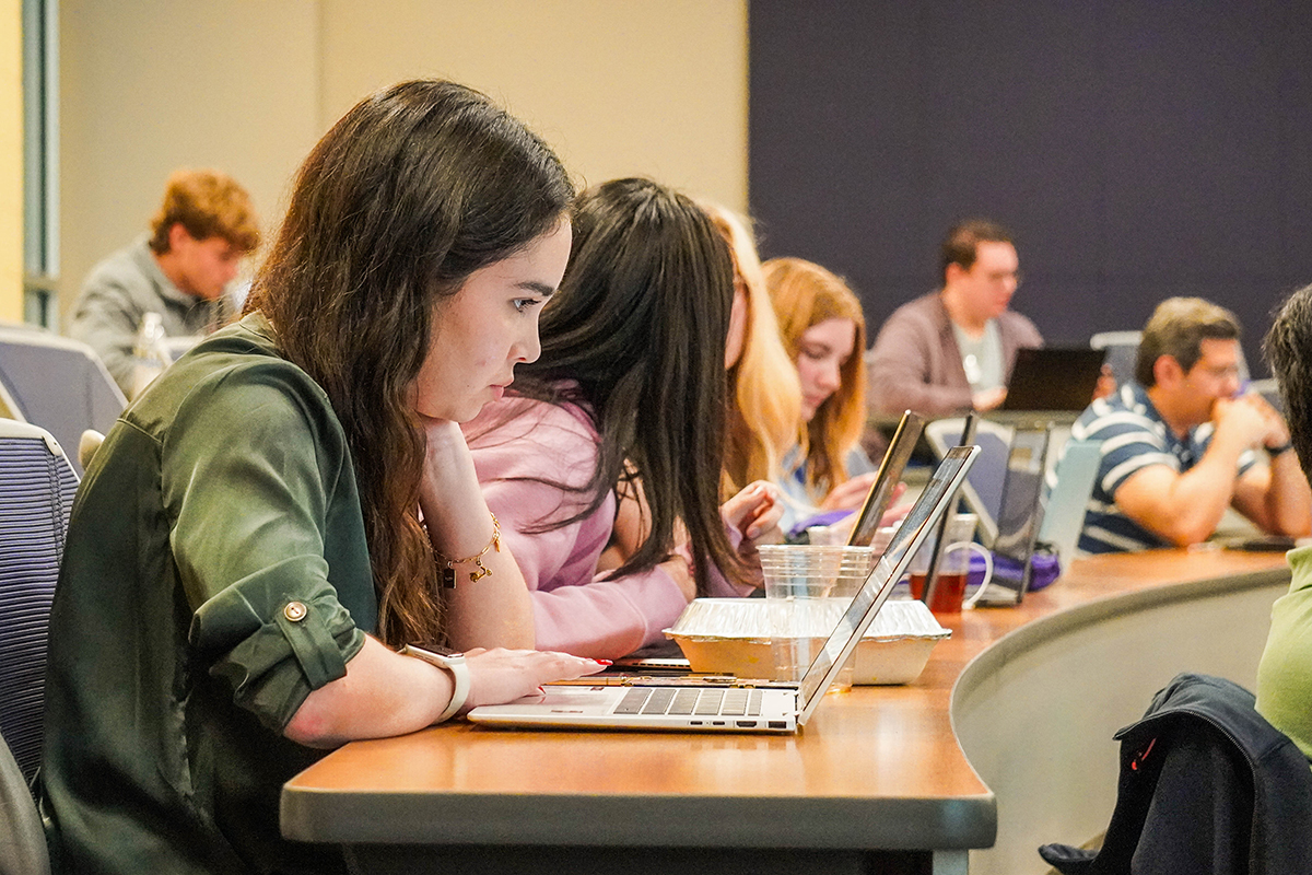 Rows of students deep in thought, looking at their laptop screens, in a college lecture hall.