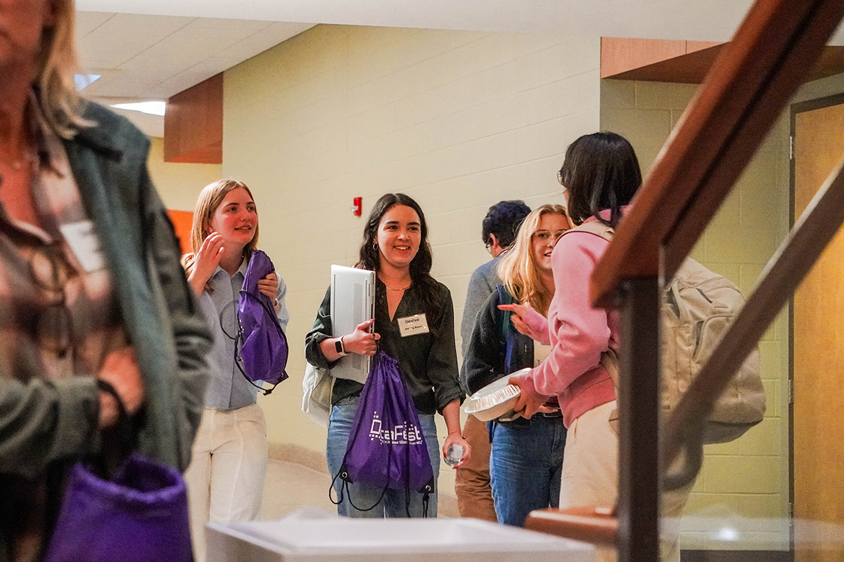 Four students gather in a huddle. They are smiling with laptops, food and DataFest swag in hand.
