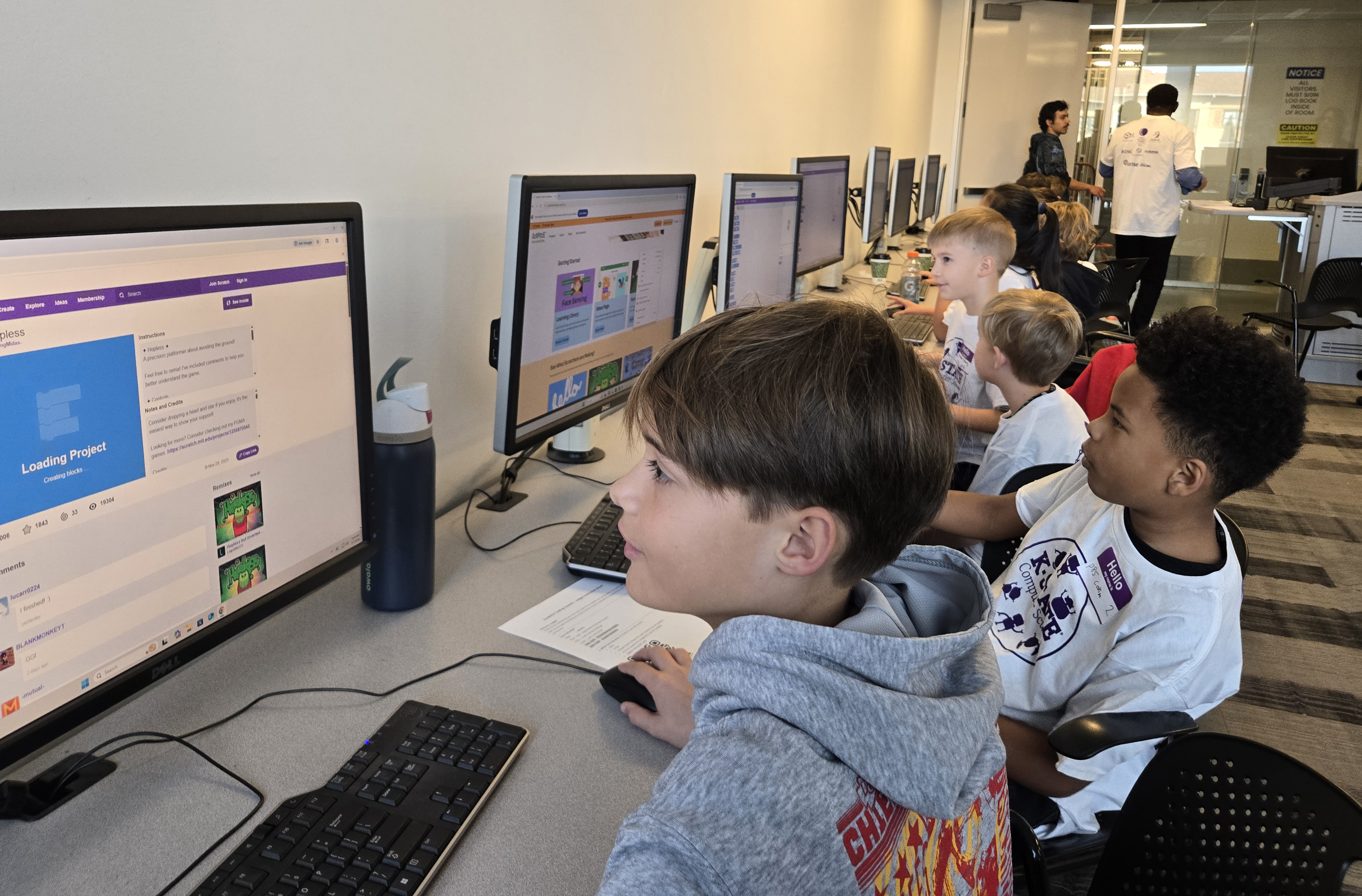 A group of elementary-school-aged boys work on computers in a college classroom.