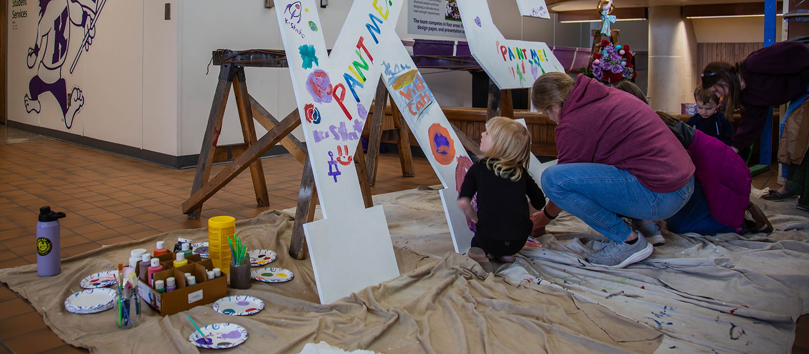 A child and her mother paint a big pair of white "K and S" letters in a college hall's atrium.