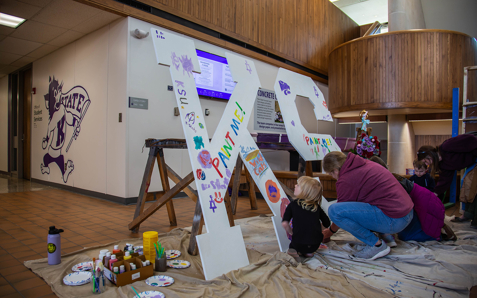 A child and her mother paint a big pair of white 