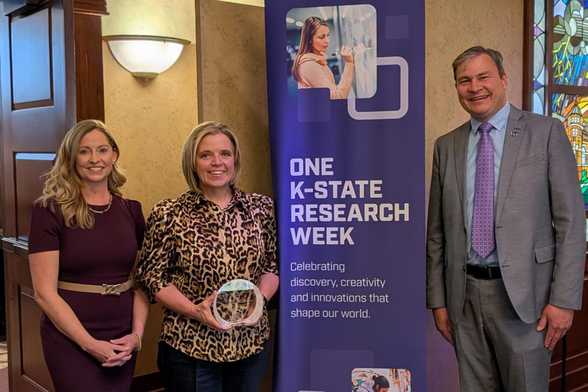 Jessica Gnad, Jill Zimmerman and Hans Coetzee smile for a photo next to a tall purple banner. 