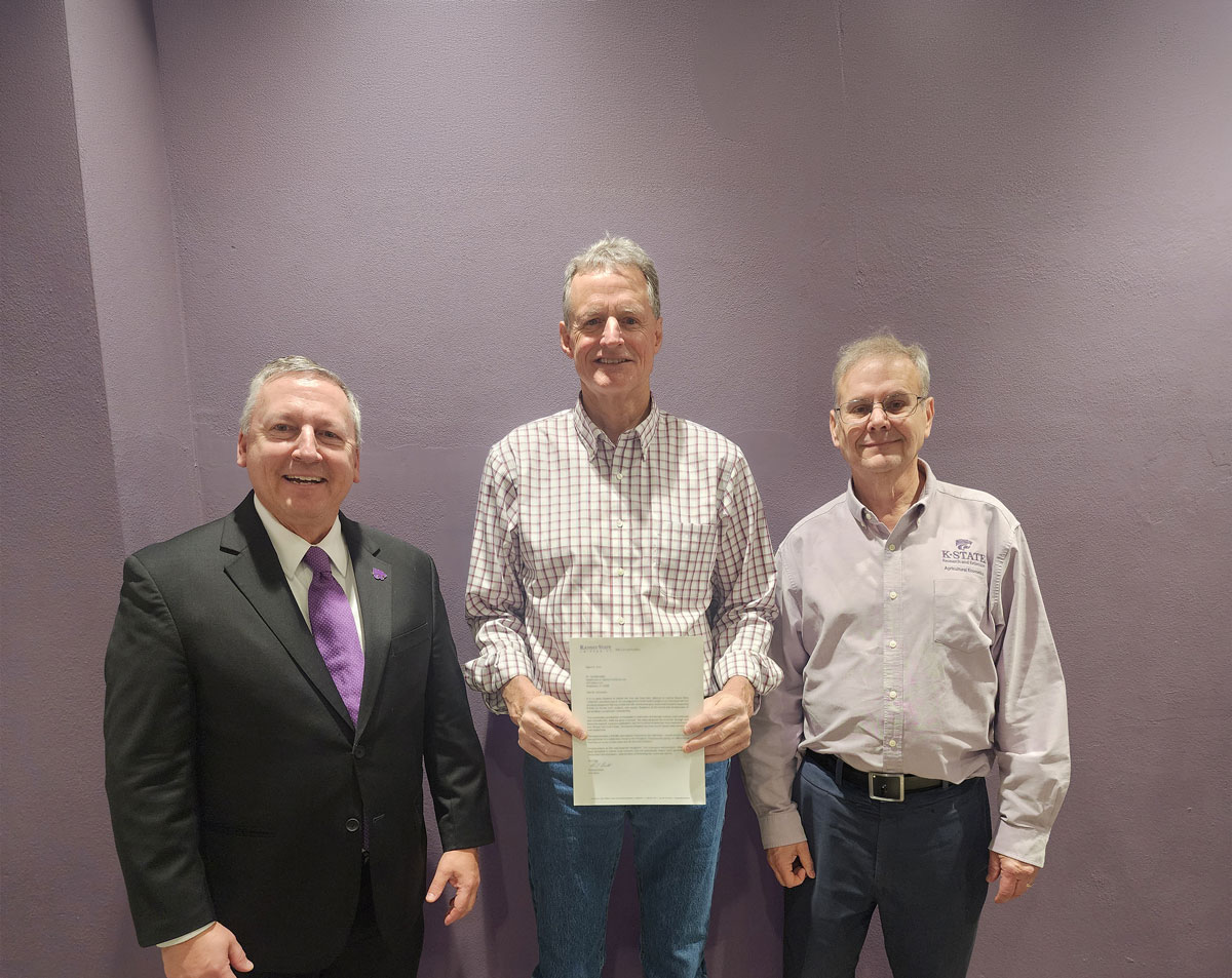 Three people pose for a photo. A person in the middle holds a piece of paper.
